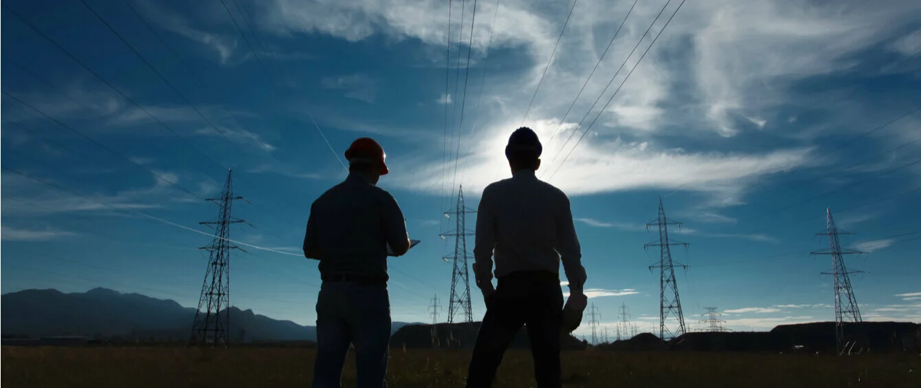 Stimmungsbild Silhouetten zweier Ingenieure vor Strommasten und bewegtem Himmel