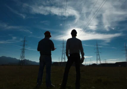 Stimmungsbild Silhouetten zweier Ingenieure vor Strommasten und bewegtem Himmel