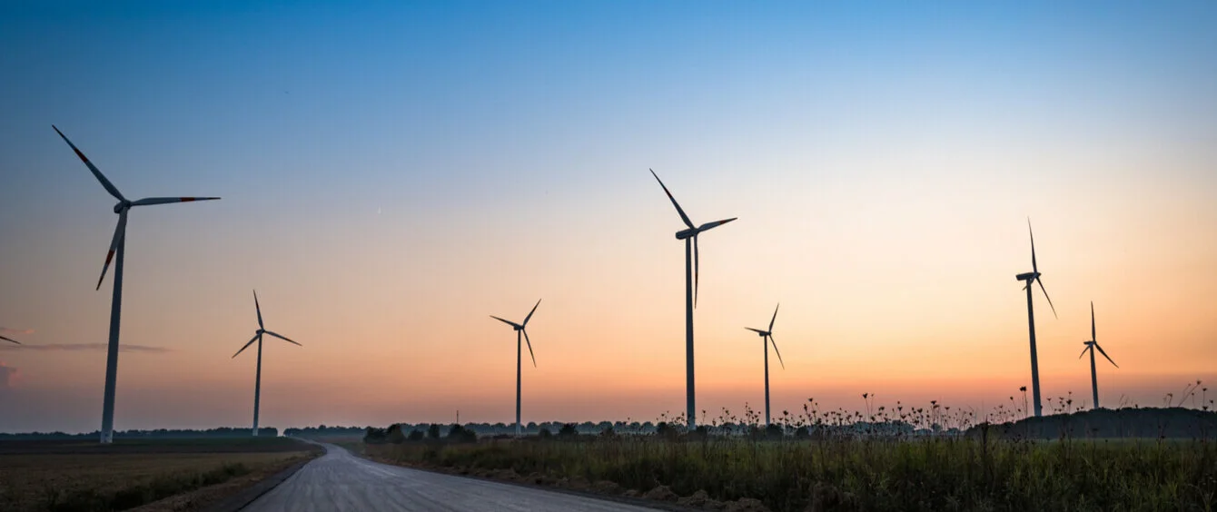 Windräder links und rechts einer Straße bei untergehender Sonne