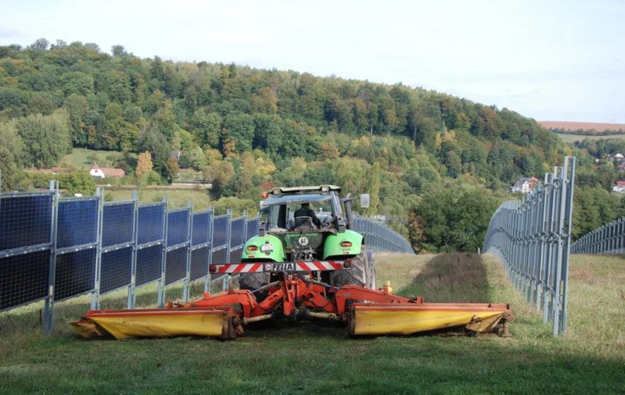 Traktor-von-hinten-bei-Mäharbeiten-zwischen-den-Modulen_885x560