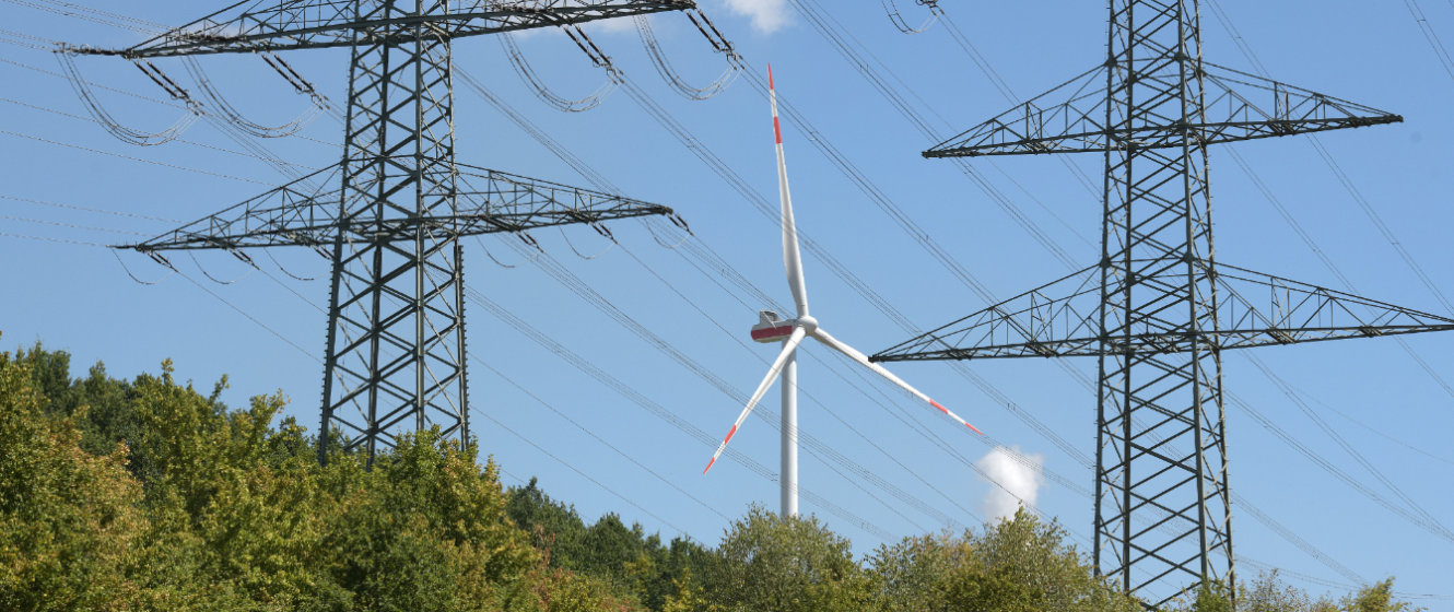 Das Bild zeigt ein Windrad und Freileitungsmasten. Erneuerbare Energie werden den Strommarkt dominieren.