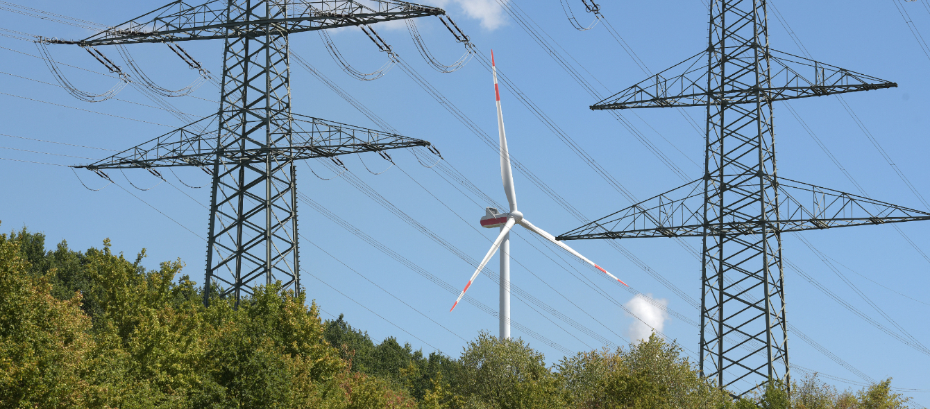 Das Bild zeigt ein Windrad und Freileitungsmasten. Erneuerbare Energie werden den Strommarkt dominieren.