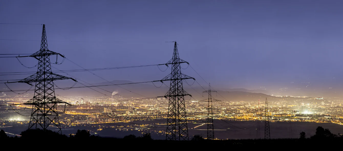 Foto, dass Stromleitungen vor einer Großstadt im dunkeln zeigt