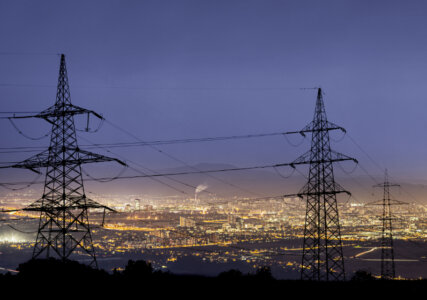 Foto, dass Stromleitungen vor einer Großstadt im dunkeln zeigt